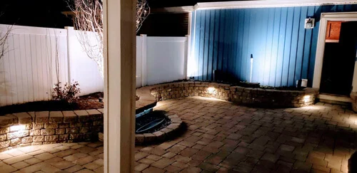 Nighttime backyard patio with lit stone walls