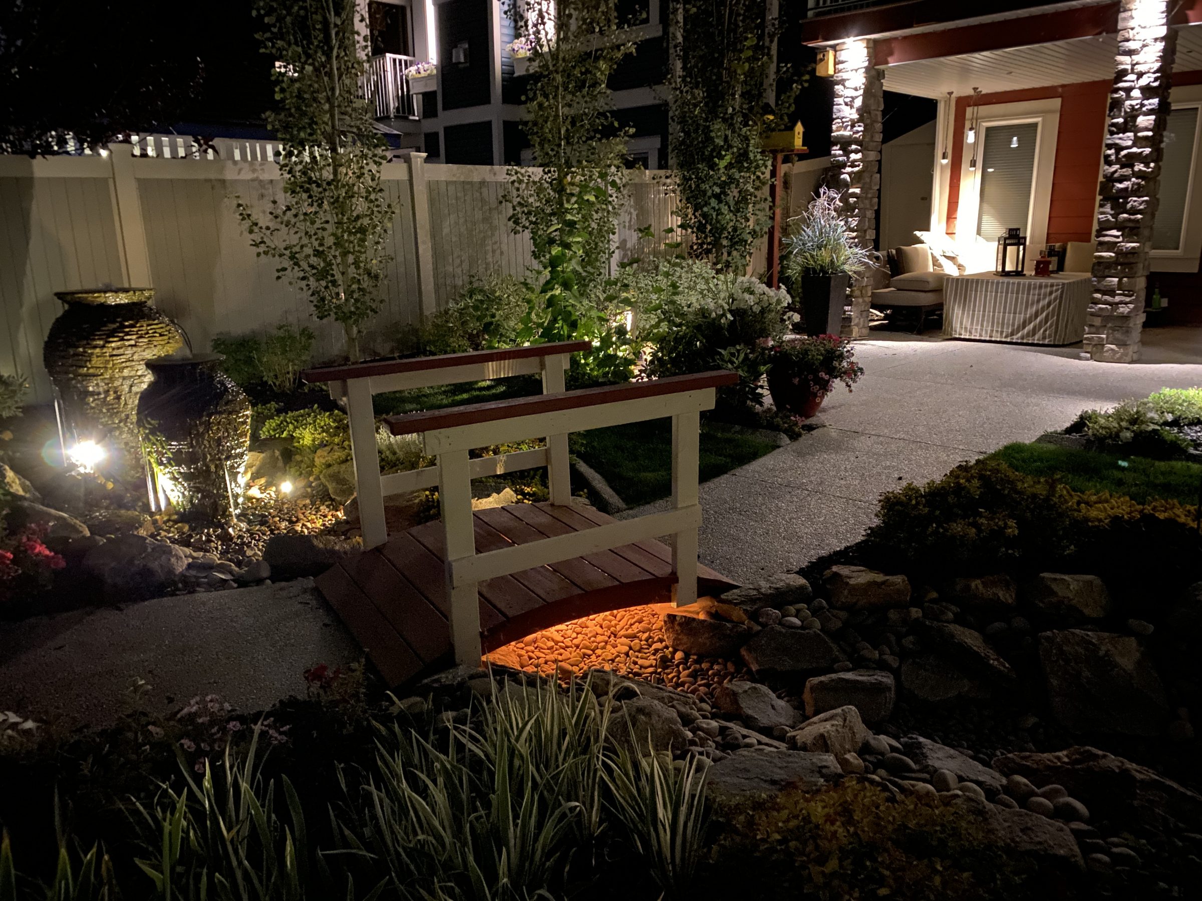 Illuminated backyard garden with small wooden bridge at night