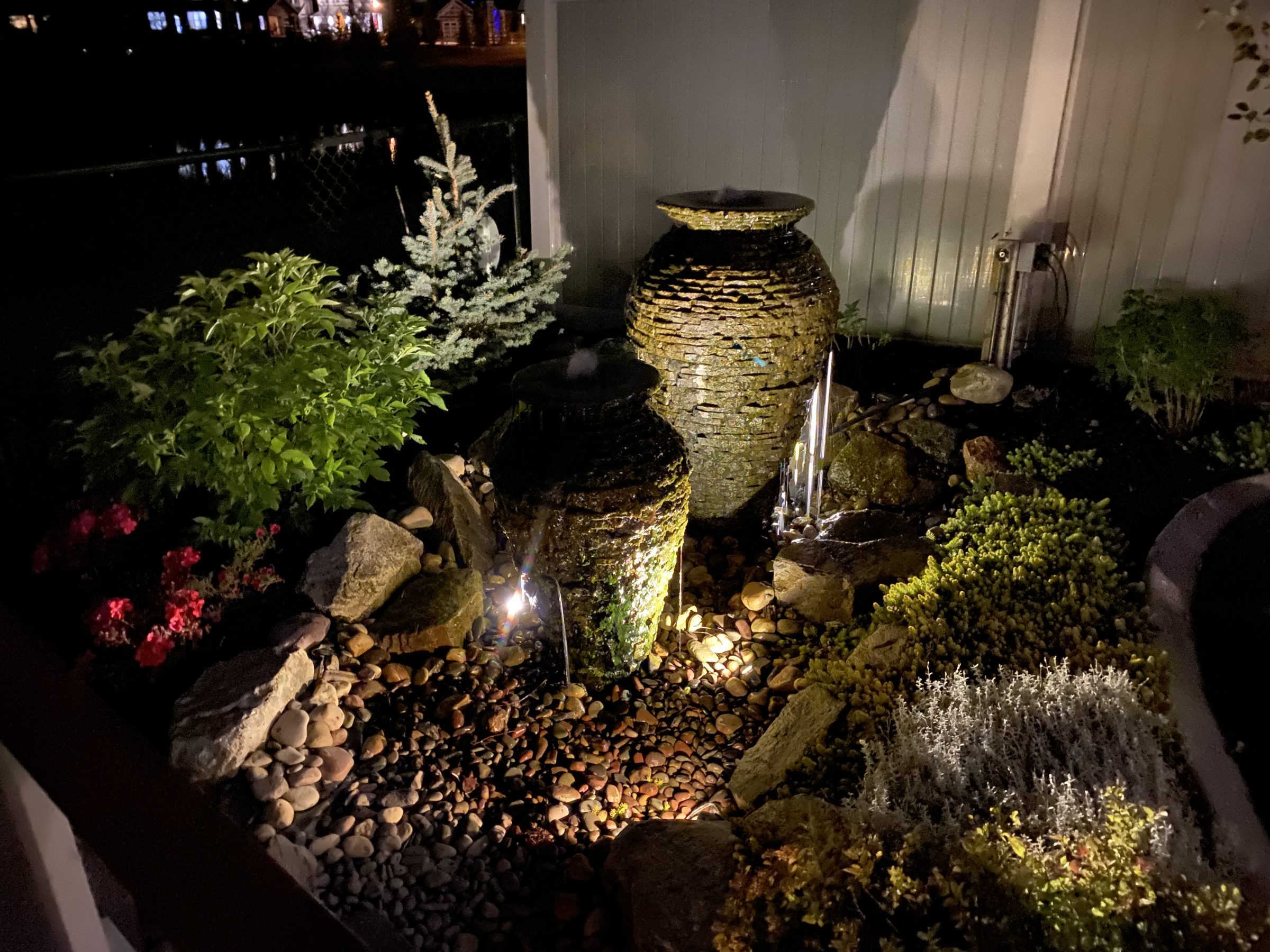 Illuminated backyard fountain with rocks and plants at night