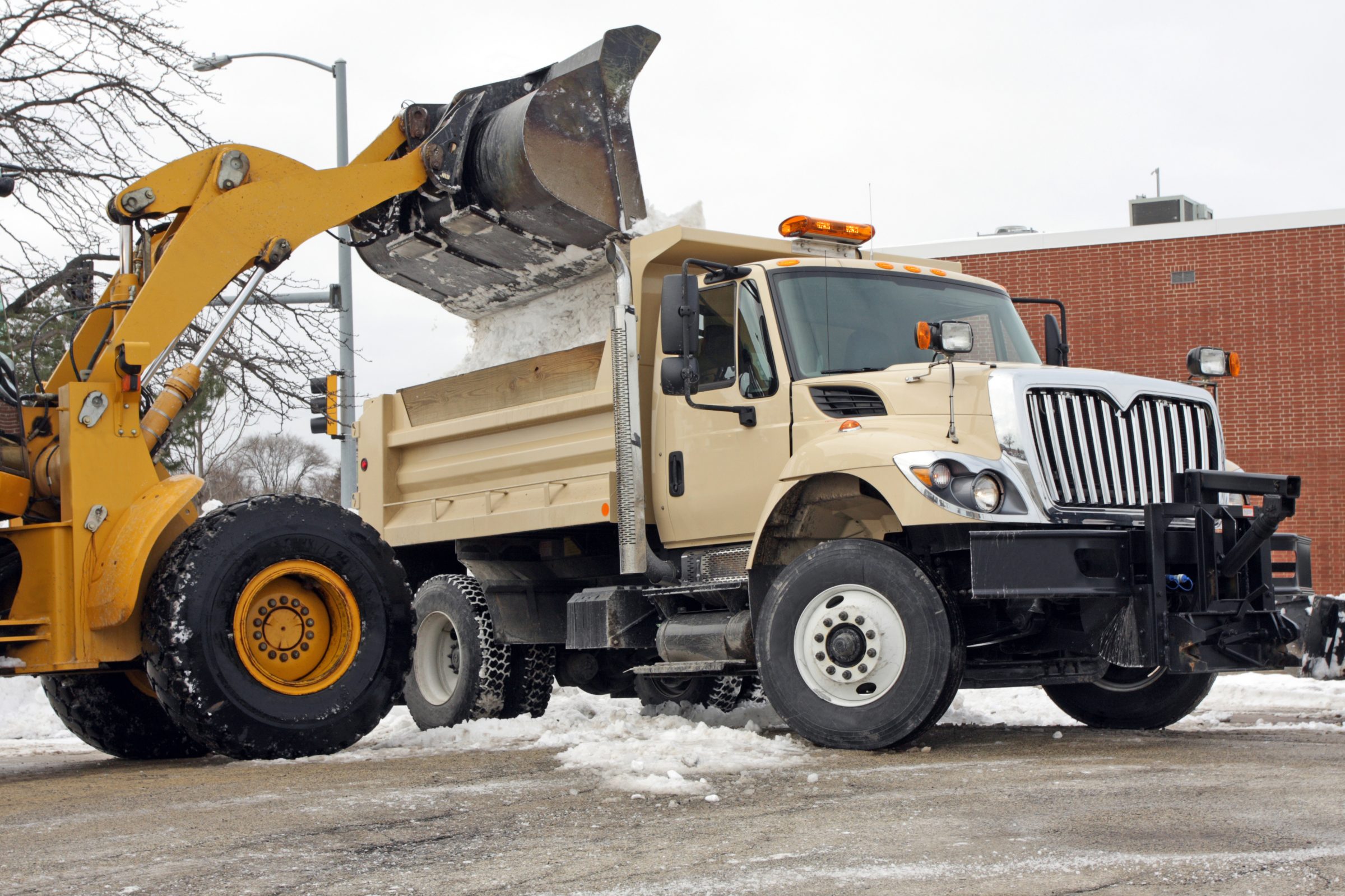 Front-end loader dumping snow into dump truck