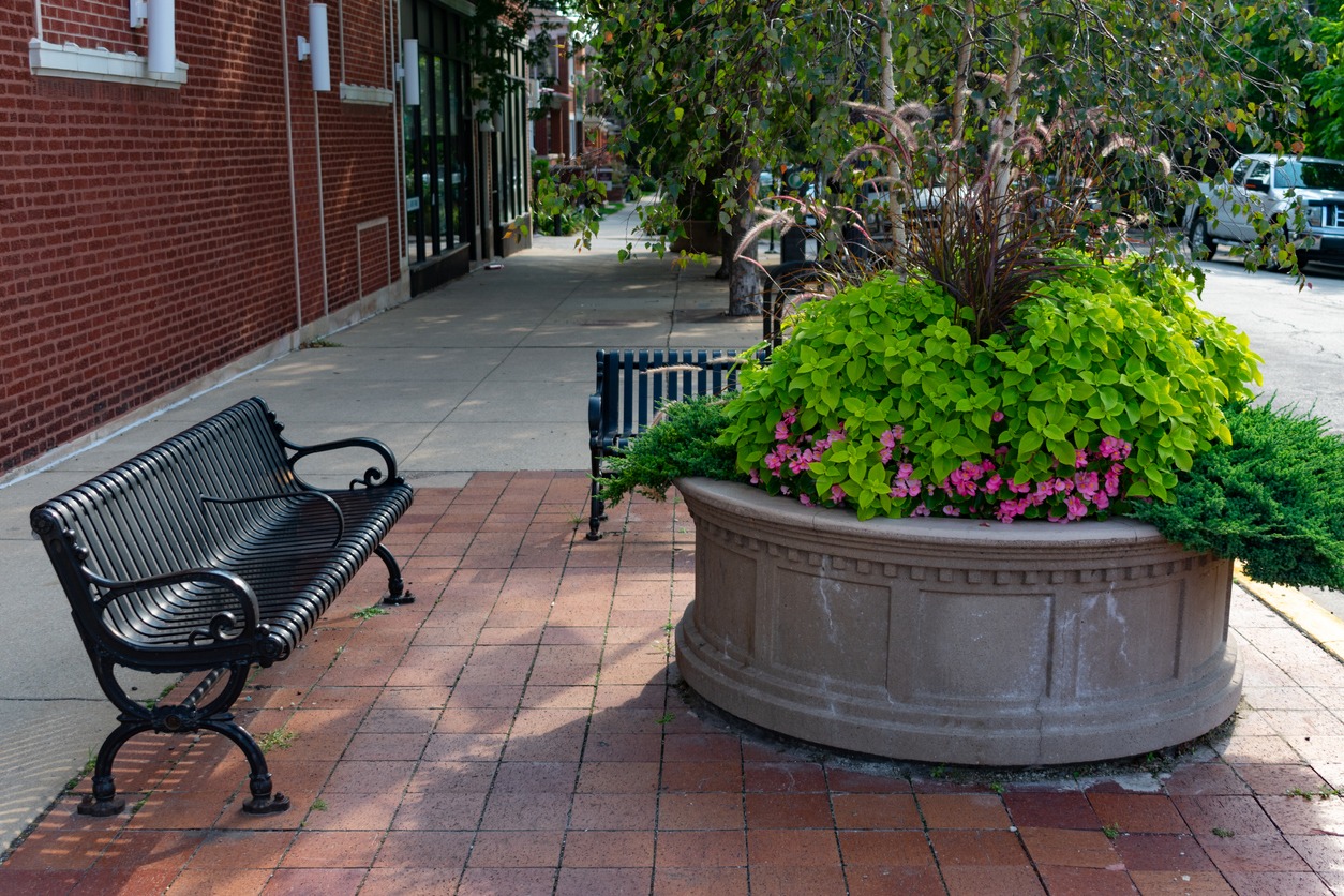Sidewalk benches beside large planter with flowers