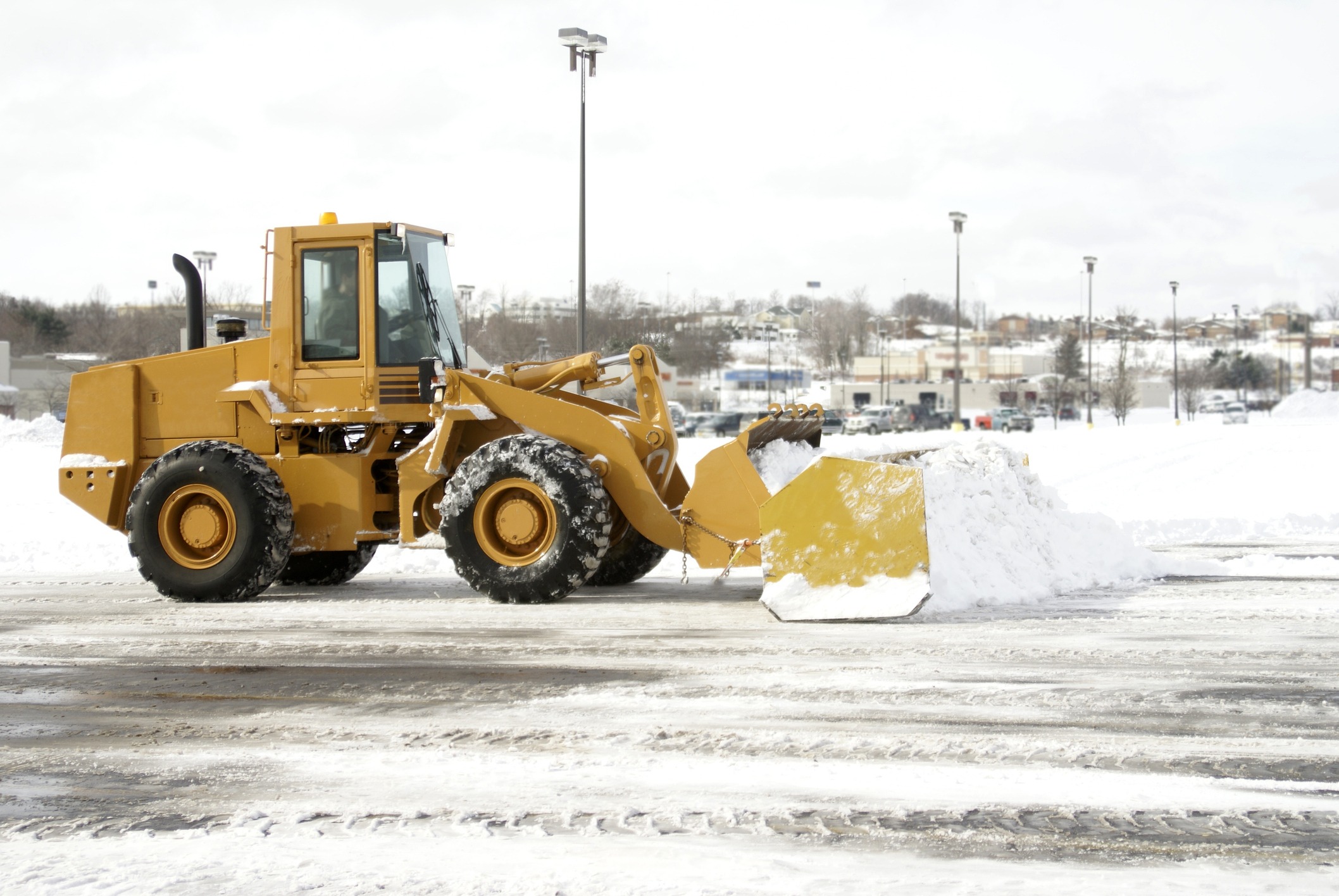 Yellow front-end loader clearing snow in parking lot