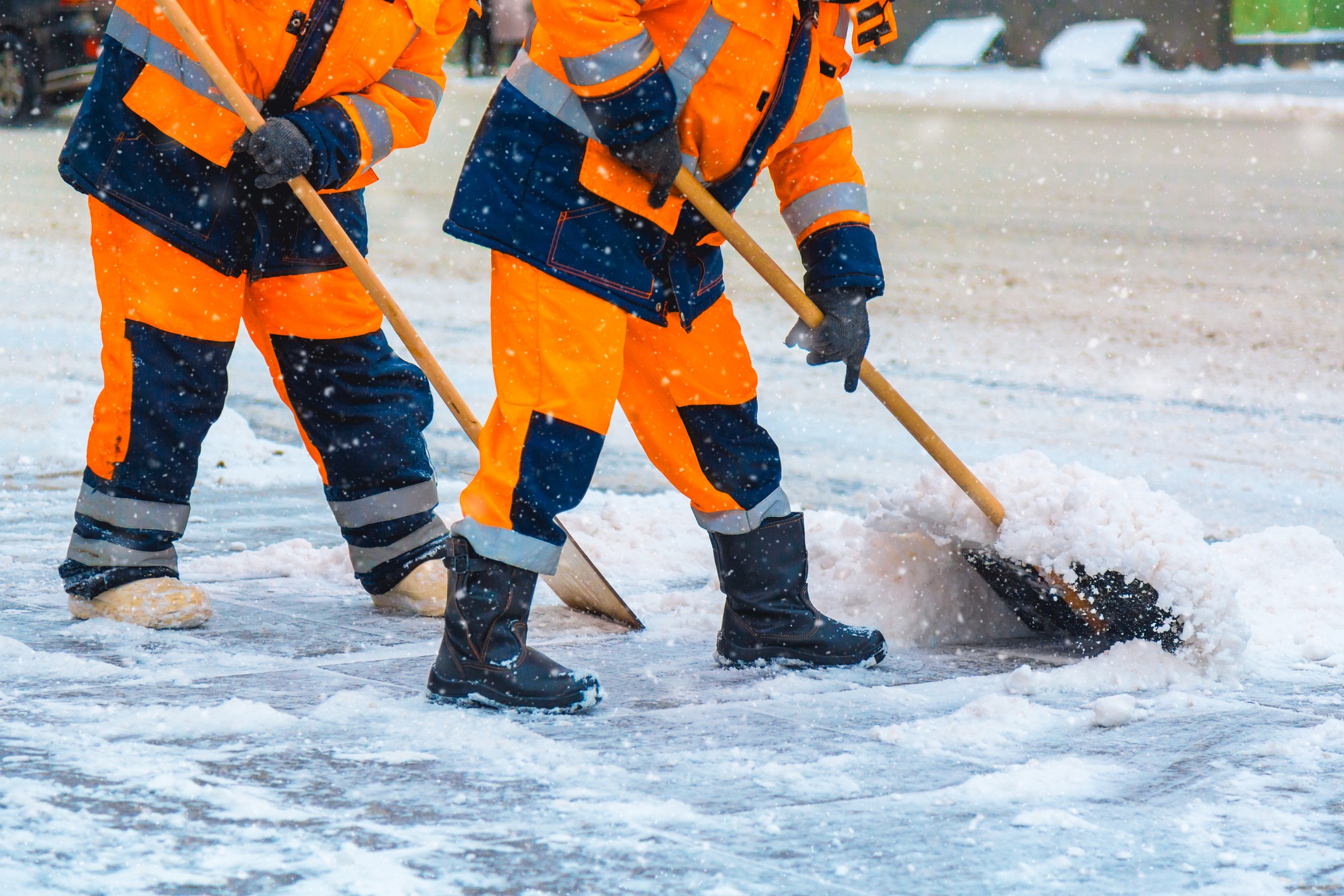 Workers in orange uniforms shoveling snow outdoors