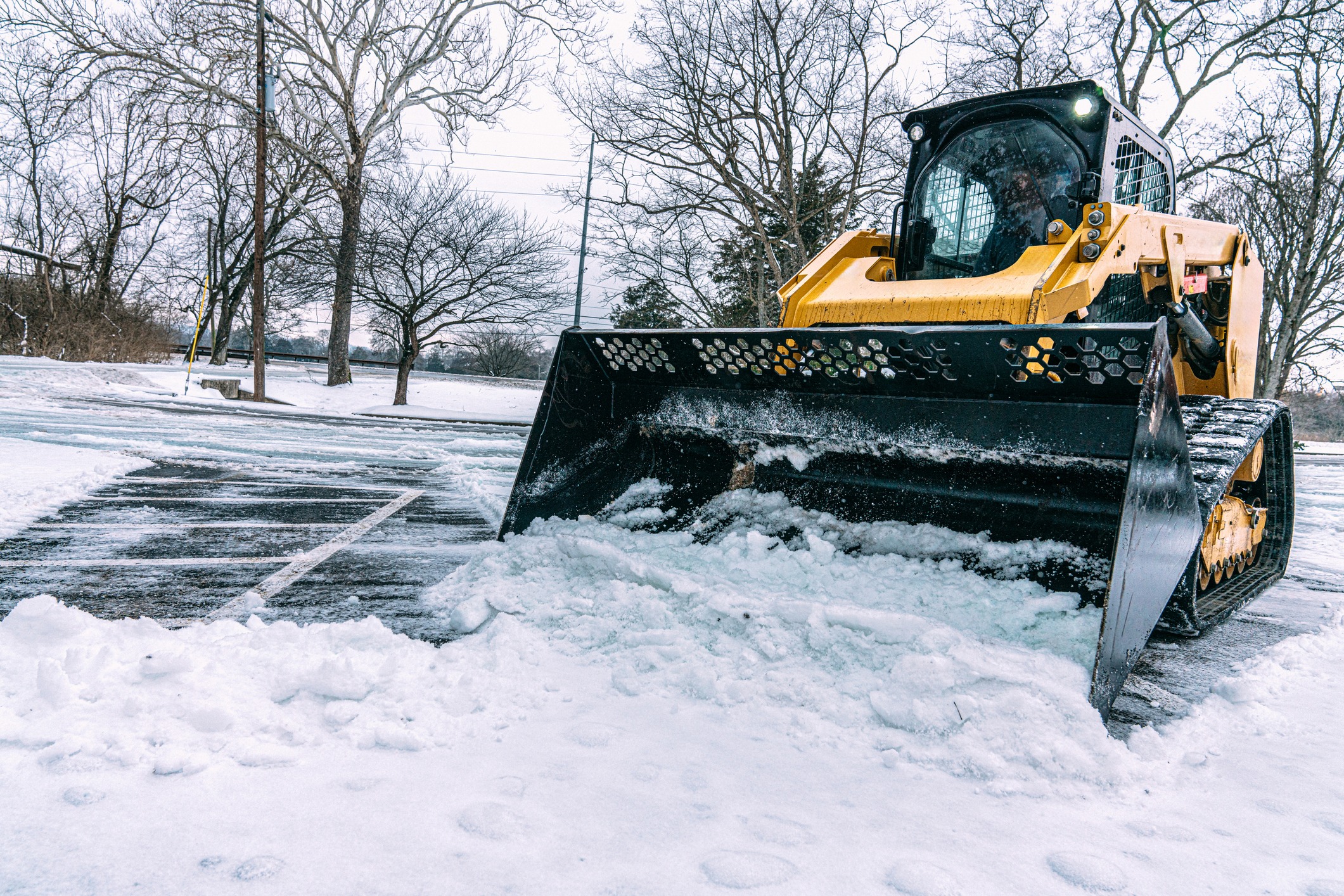 Skid-steer loader plowing snow in parking lot