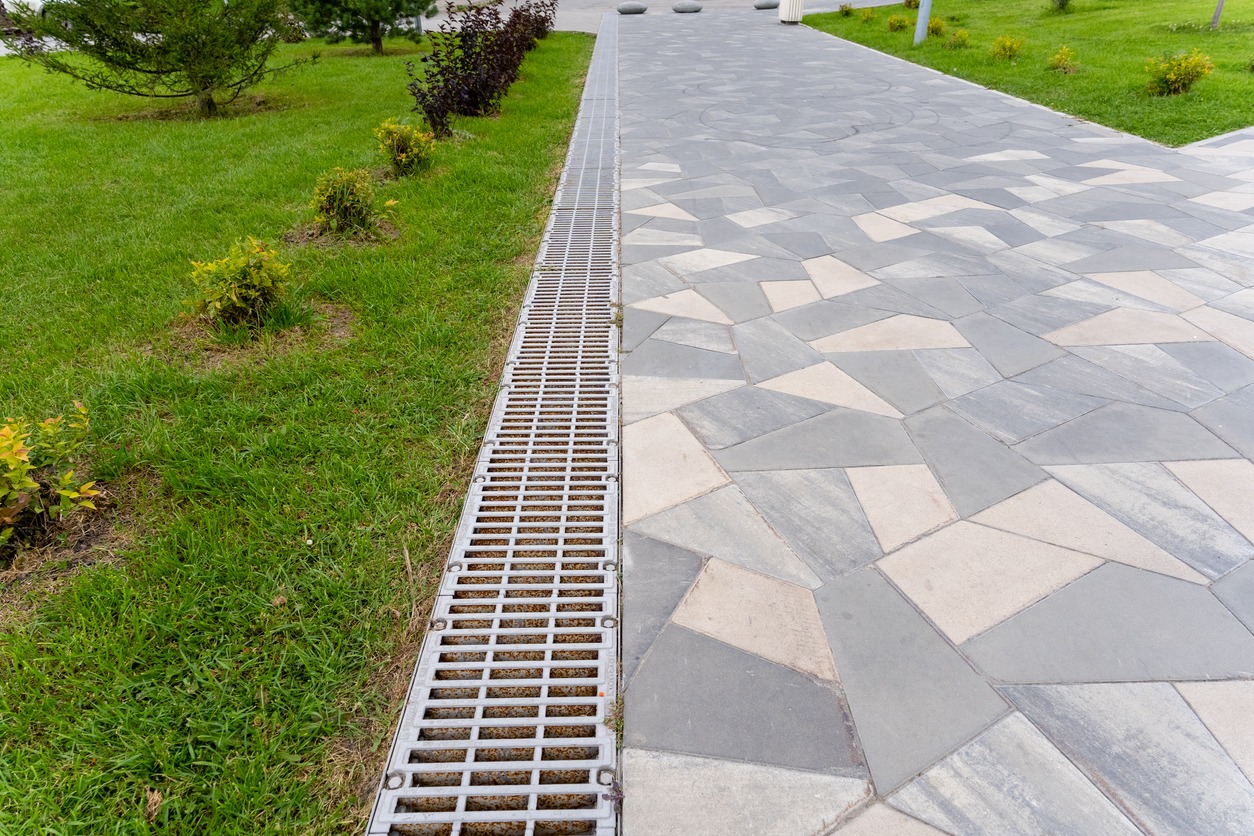 Paved walkway with metal drainage grate beside grass