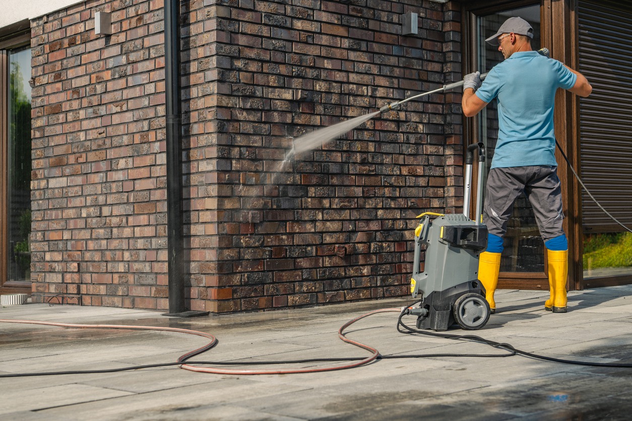 Man pressure washing brick house exterior wall