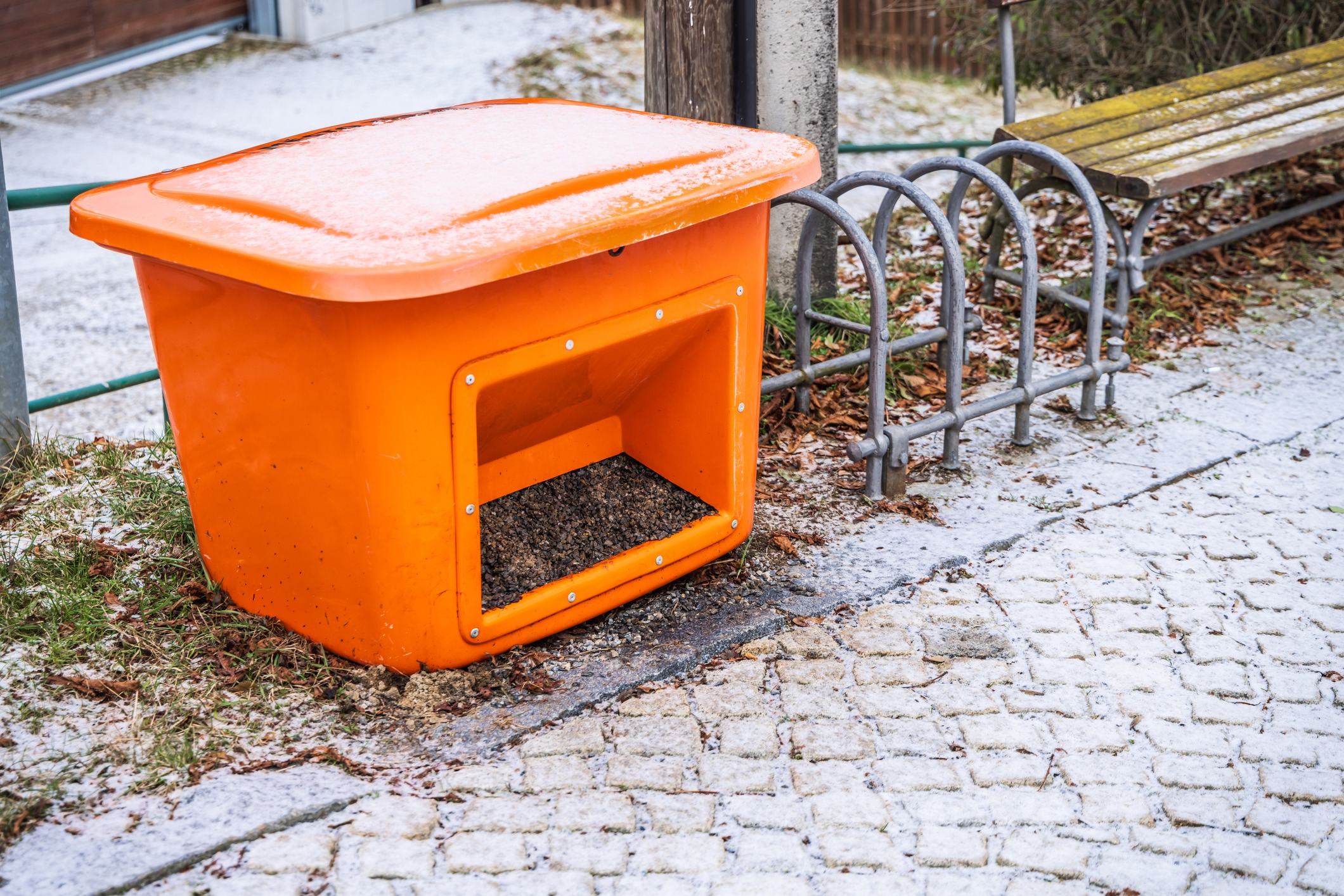 Orange road salt bin on snowy sidewalk