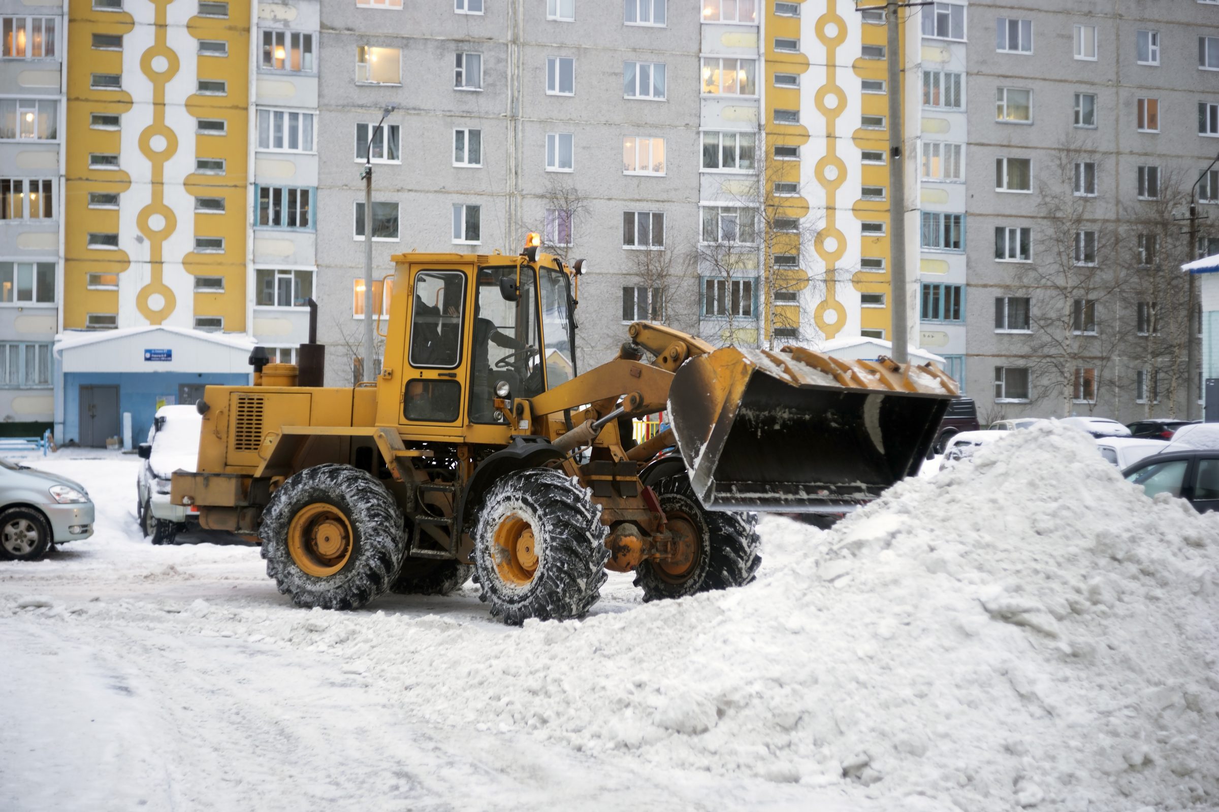 Yellow loader clearing snow near apartment buildings